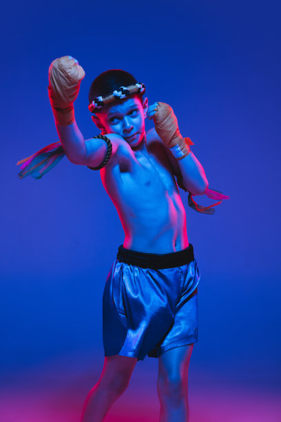 年轻的男孩泰国拳击手训练在霓虹灯的蓝色背景。图片下载