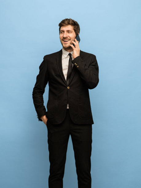 年轻快乐的男子在黑色西装孤立的蓝色背景肖像。图片下载