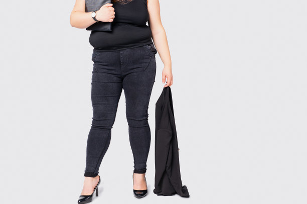 裁剪照片超重女性的腿。大尺寸模特女孩穿着正式的西装和黑色的鞋子站孤立的灰色背景。XXL模特女人在正式的服装摆姿势全长。图片下载