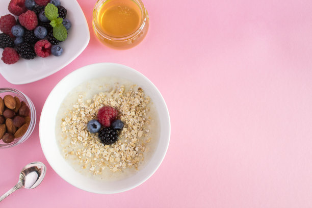 早餐:粉红色背景上有浆果、蜂蜜和坚果的燕麦粥。前视图。副本的空间。图片下载