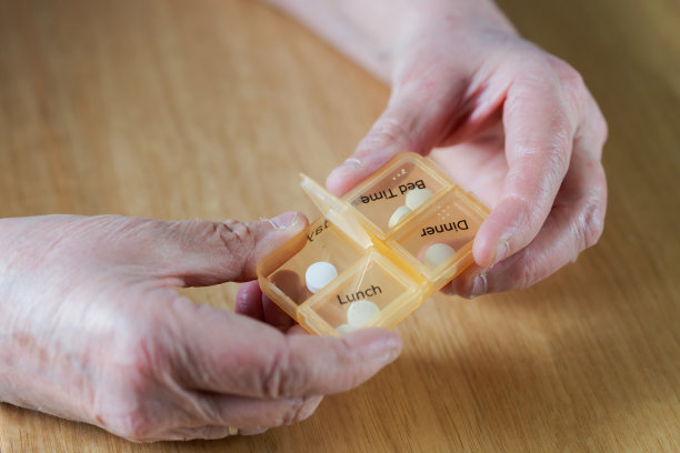 一个老年妇女的手的特写服用她的药在一个药丸盒子在木桌上的一周，商业，健康的概念图片下载