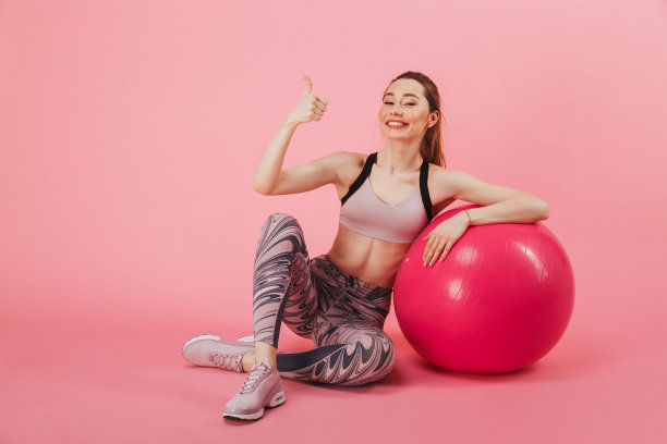 快乐的女运动员坐在地板上拿着健身球图片下载