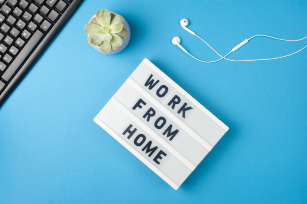 从家里工作-文本显示灯箱在蓝色背景的工作场所。黑色键盘和白色耳机。自由职业的概念图片下载