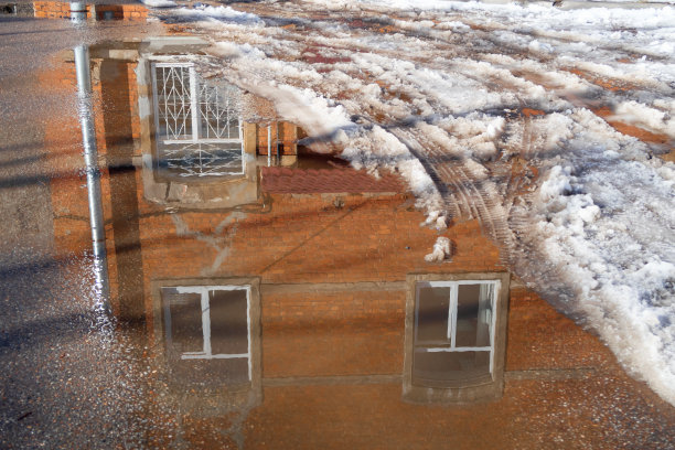 早春的城市街道上有融雪和水坑与倒影的建筑图片下载