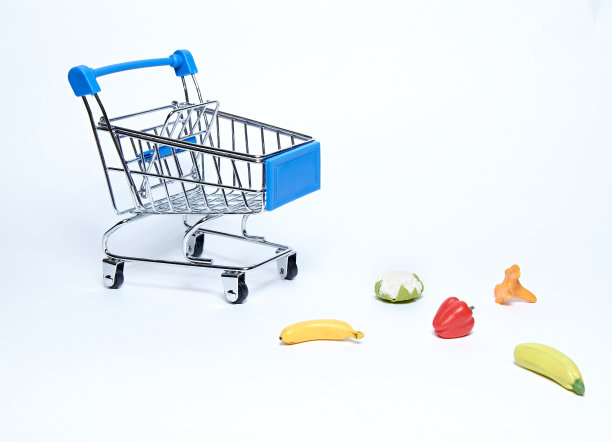 一辆蓝色的超市购物车，在孤立的白色背景下，散落着水果和蔬菜。图片下载