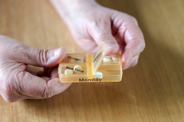 一个老年妇女的手的特写服用她的药在一个药丸盒子在木桌上的一周，商业，健康的概念图片下载