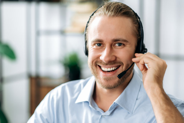 特写英俊的胡子满意的男人，呼叫中心接线员或商业领袖。白人商人戴着耳机，穿着正装，看着镜头，友好地微笑着素材图片