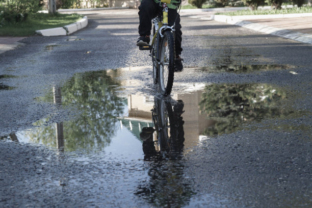 一个男人在路上骑自行车。雨后沥青路上的水坑。飞溅的水花和水滴从车轮下飞溅图片下载