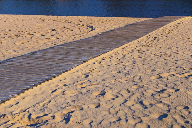 一条木制的小路穿过沙滩通向大海。金色沙滩上的木地板。通往海滩的木栈道的细节。阳光明媚的午后，水公园内的第聂伯罗河景观。基辅,乌克兰图片下载