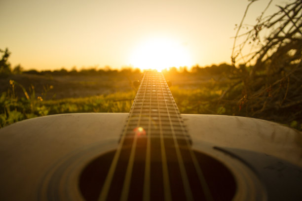 在日落时弹吉他。和朋友们在大自然的黄金时间弹吉他，就在夜幕降临前的一个小时。吉他上的日落图片下载