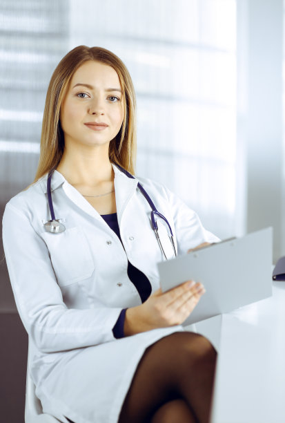 一位年轻乐观的女医生正坐在诊所橱柜的办公桌前，用着写字板。友好的女医生的肖像妇女与听诊器。医院里完美的医疗服务。医学的概念图片下载