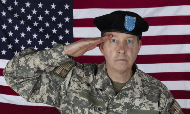 一名男子正在敬礼，穿着军服和贝雷帽，背景是美国国旗图片下载