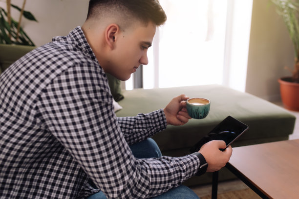 男人用黑屏和咖啡杯阅读智能手机。模糊的背景图片下载