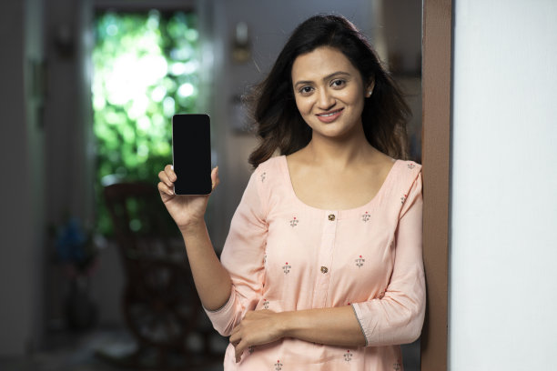 一名年轻女子的照片显示手机空白屏幕，她站在门口附近:库存照片图片下载