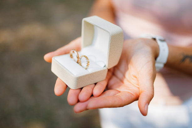 女人拿着一个白色的盒子，手里拿着金婚戒，特写图片下载