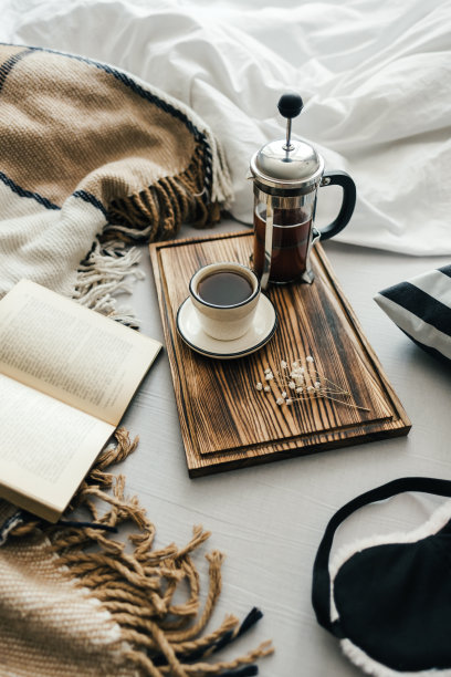 在床上打开书，咖啡是用法式压壶和杯子煮的，放在木板上。早上在家，舒适舒适。图片下载