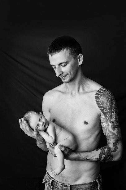 4. 手臂上有纹身的父亲抱着黑白背景上的新生儿图片下载