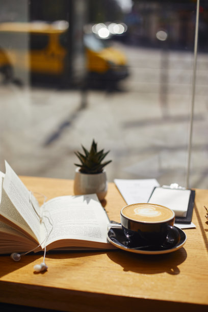 一杯咖啡和一本书在咖啡馆靠近窗户的桌子上。黑杯卡布奇诺或拿铁。阳光灿烂的日子图片下载