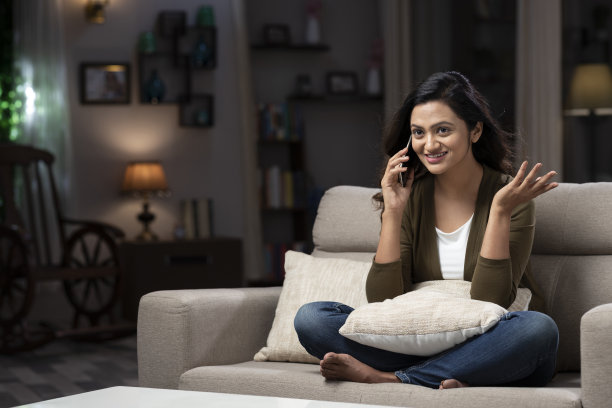年轻女子坐在家里的沙发上打电话:-库存照片图片下载