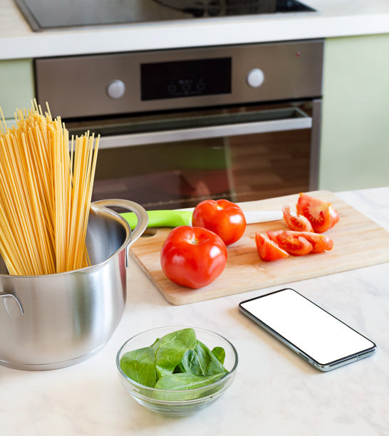 厨房桌子上有番茄和菠菜通心粉的配料和智能手机图片下载