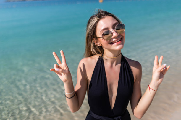 在阳光明媚的海滩上休息时，穿着胸罩的微笑女子打着和平手势，自拍照片图片下载