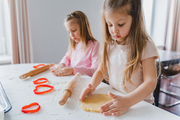 小女孩们，姐妹们在为情人节做自制的心形饼干。情人节。礼物，给妈妈的惊喜。红色模具，擀面杖，面粉，面团。手工家庭，带孩子的面包店图片下载
