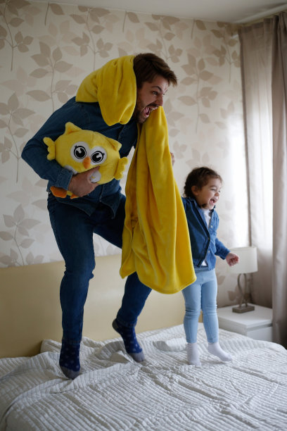 快乐的爸爸和可爱的女儿跳在床上的照片图片下载