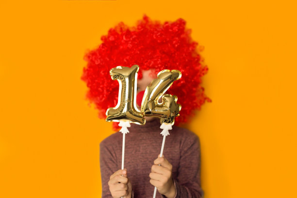 四月一日愚人节的概念。情人节快乐。鲜红的丘比特在情人节。有趣的女孩小孩小丑玩金色14气球孤立黄色背景。图片下载