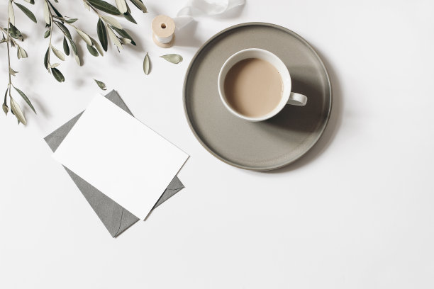 空白贺卡，信封模型。一杯咖啡，橄榄枝和丝带孤立在白色的桌子背景。夏日婚礼，早餐静物作文。平躺，俯视图。图片下载