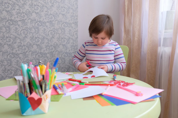 一个小女孩画，画，剪出一颗心。孩子们的创造力。情人节，母亲节，父亲节的礼物。在家封闭隔离期间上课/一个孩子在桌子上画了一个心形的相册和胶水贴纸。一个小女孩画图片下载