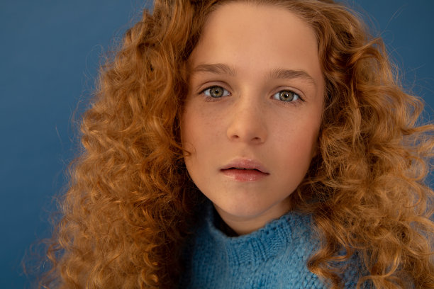 蓝色背景下的红色卷发女孩。雀斑的脸。青少年染发、护肤。特写照片图片下载