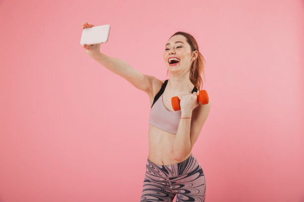 女运动员一边用智能手机自拍一边拿着哑铃锻炼图片下载