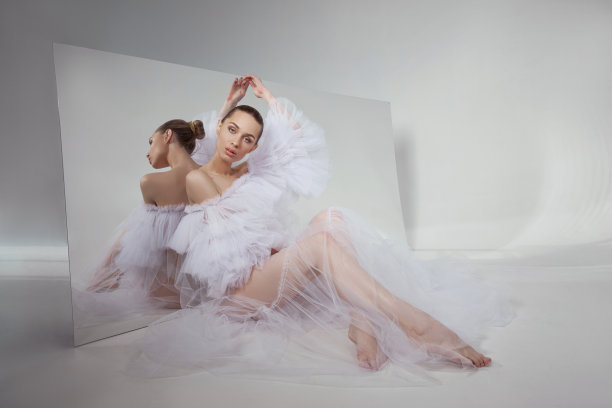 浪漫的美女穿着一件轻盈透明的连衣裙，坐在地板上反射着柔韧的镜子。完美的身体和长腿图片下载