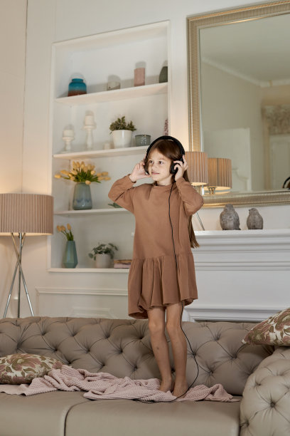 女孩在家里玩得很开心，在沙发上跳来跳去。孩子戴着耳机跳舞和听音乐图片下载