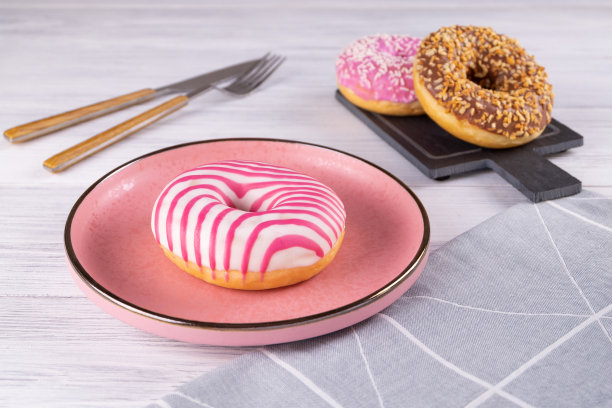 三个裹着糖衣的甜甜圈放在一个粉色的陶瓷盘子和一块石板上图片下载