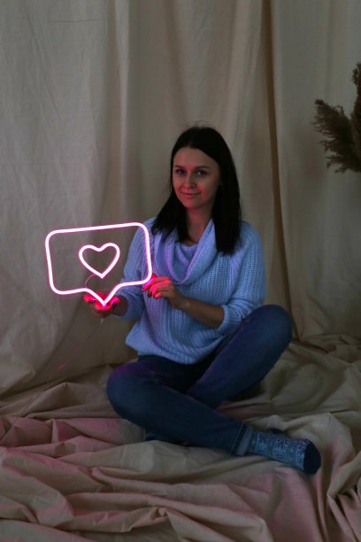 拿着霓虹灯的漂亮女孩。霓虹标志粉色的心。时尚的风格。情人节。图片下载