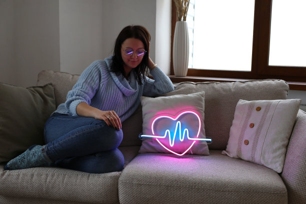 拿着霓虹灯的漂亮女孩。霓虹标志粉色的心。时尚的风格。情人节。图片下载