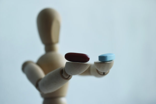一个木制的男人雕像，拿着两粒药丸，在明亮的背景上有自由的空间给你的文字。医学和保健概念。图片下载
