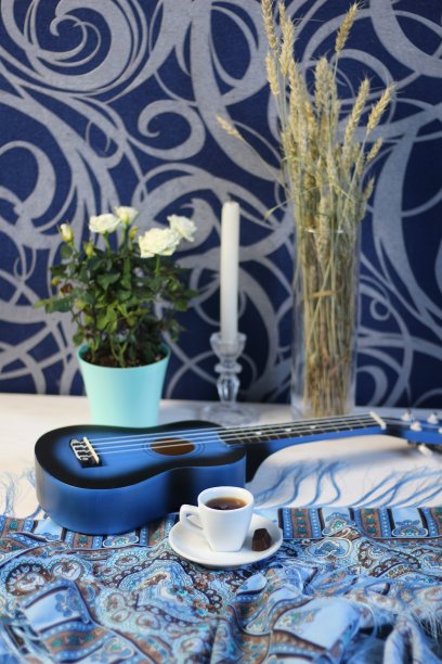 一杯咖啡，巧克力，蓝色背景的白色桌子上的尤克里里吉他，玫瑰，蜡烛，干麦穗图片下载