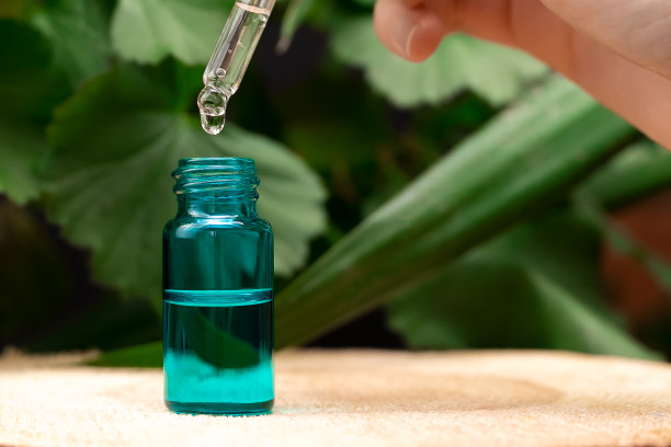 一个女人的手拿着一个眼药水在一瓶血清上站在一个木架子上，背景是绿色植物与复制空间。美容师的概念，生态学图片下载