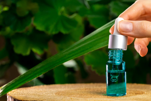 一个女人的手拿着一个眼药水在一瓶血清上站在一个木架子上，背景是绿色植物与复制空间。美容师的概念，生态学图片下载