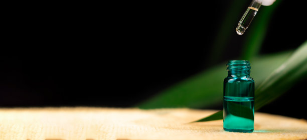 化妆移液管上方的一瓶血清在木桌上，以绿色植物为背景，黑色背景与复制空间。美容、医学的概念。横幅图片下载