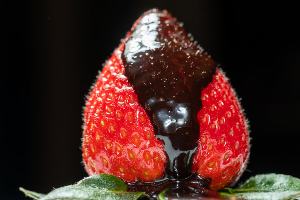 新鲜的草莓与绿色的叶子，淋上巧克力，在黑色的背景图片下载