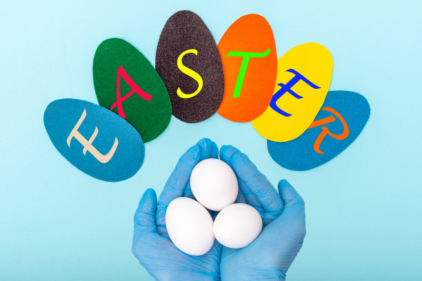 彩色纸蛋与铭文复活节和手在保护医疗手套拿白色的蛋图片下载