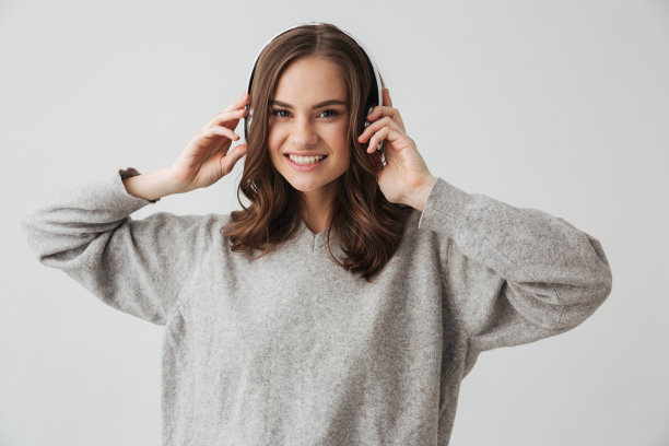 微笑的黑发女人穿着毛衣和耳机听音乐图片下载