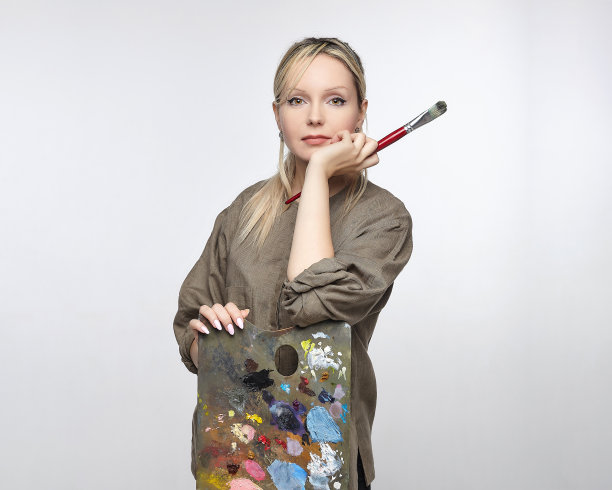 在一个白色背景的工作室里，年轻的女艺术家拿着调色板和画笔摆姿势图片下载