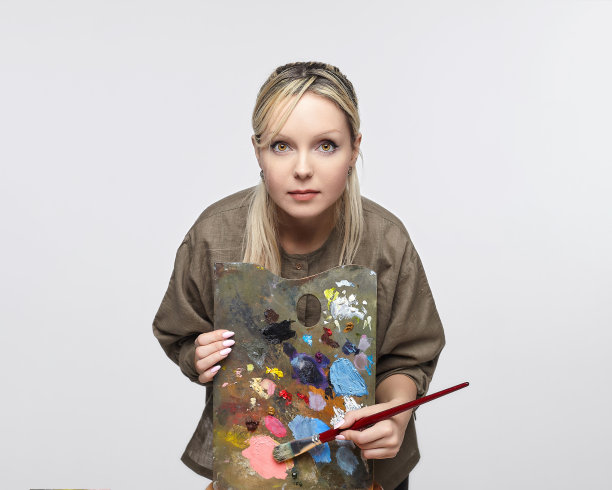 在一个白色背景的工作室里，年轻的女艺术家拿着调色板和画笔摆姿势图片下载