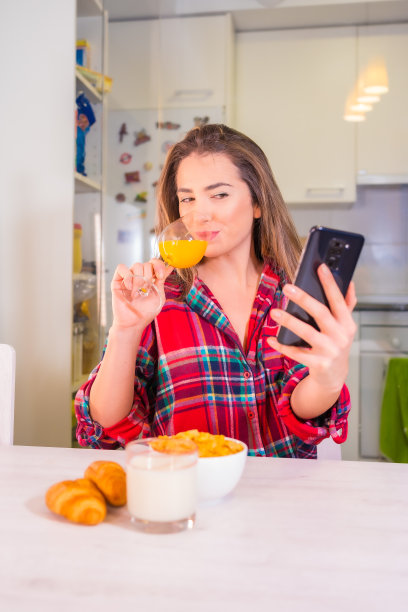 健康的生活方式，金发白种女人早餐喝橙汁，用手机自拍图片下载