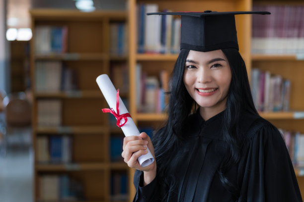 一名年轻快乐的亚洲女子大学毕业生穿着毕业礼服和帽子戴着面具持有学位证书，以庆祝她的教育成就在毕业典礼上。库存图片图片下载