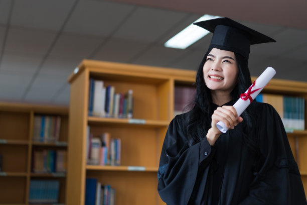 一名年轻快乐的亚洲女子大学毕业生穿着毕业礼服和帽子戴着面具持有学位证书，以庆祝她的教育成就在毕业典礼上。库存图片图片下载